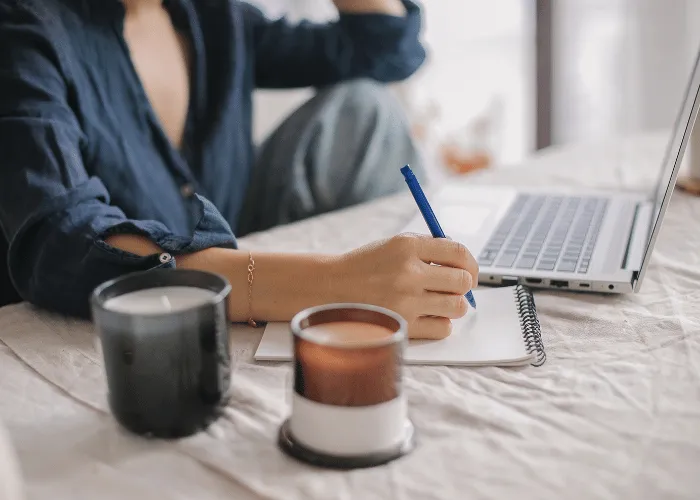 A person taking notes in a notebook next to a laptop