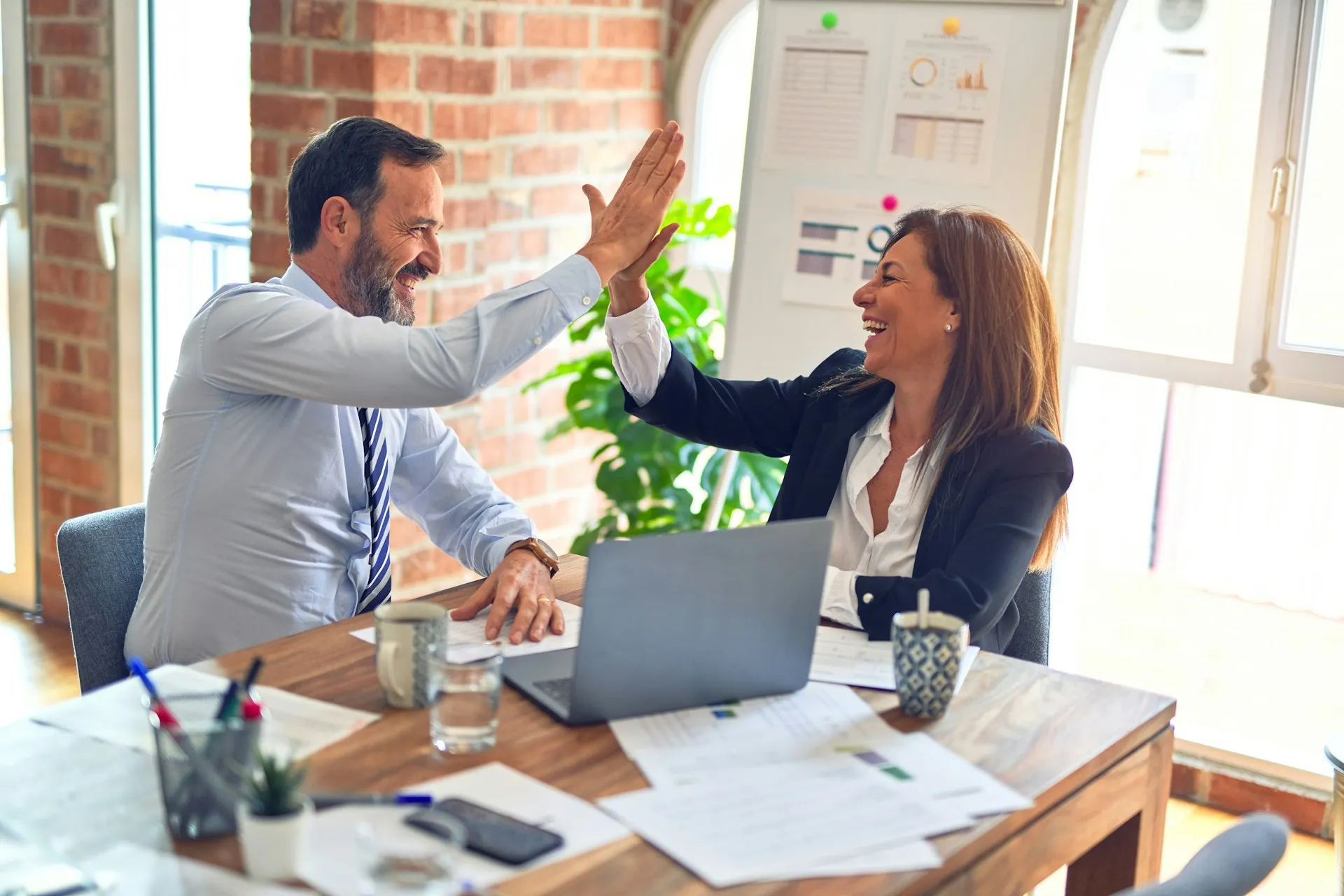Two colleagues giving each other a high five at a desk