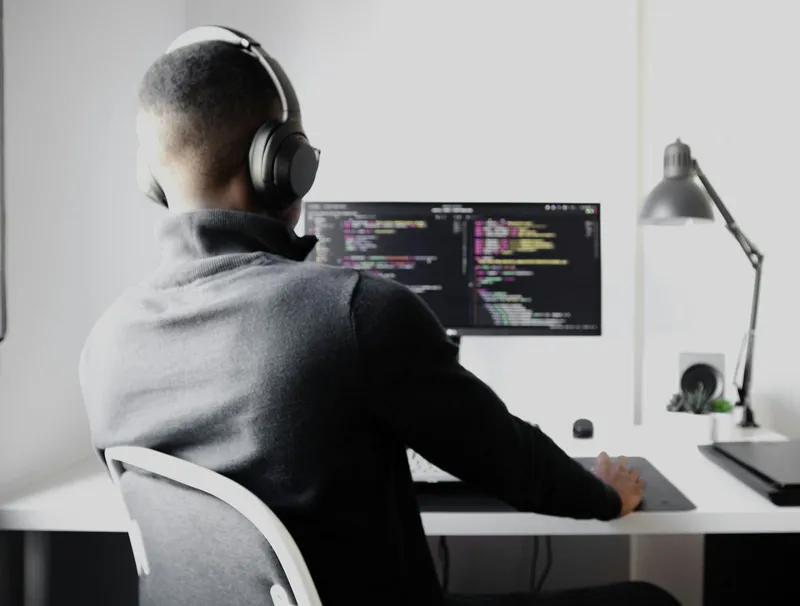 A developer wearing headphones works alone at a desk with code on the monitor