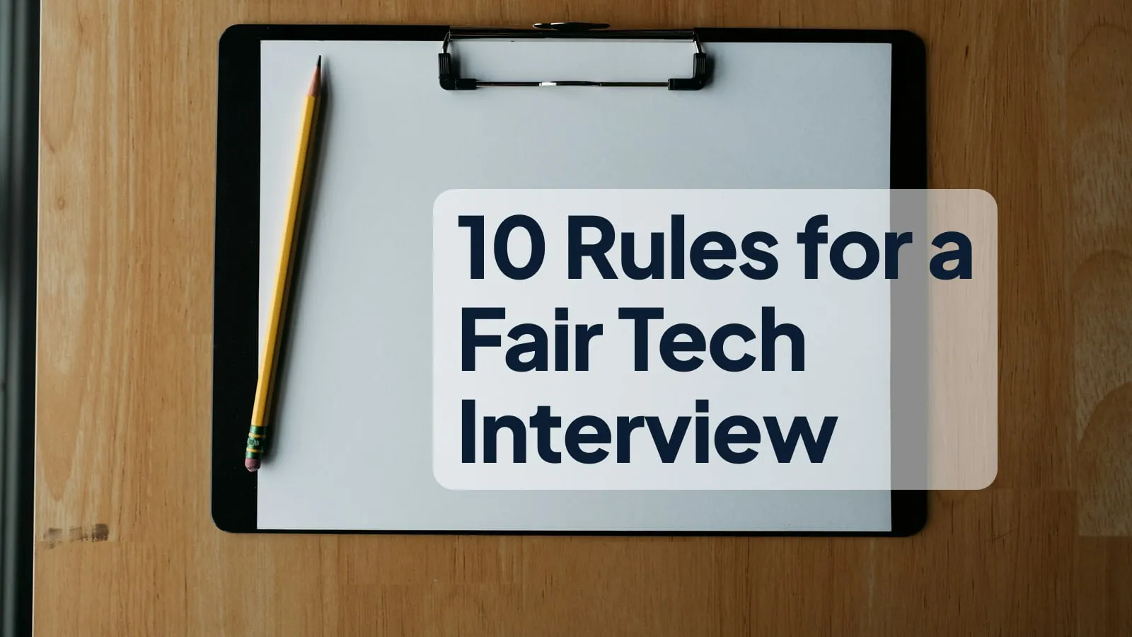 A clipboard with blank paper and a pencil on a wooden desk, with the headline "10 Rules for a Fair Tech Interview" on the paper