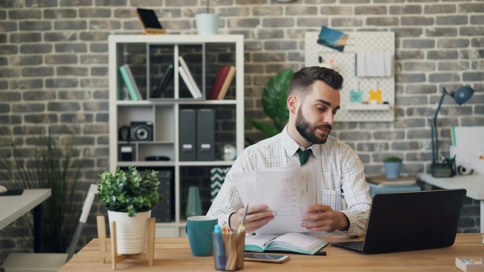 A man reviewing papers at his desk next to a laptop