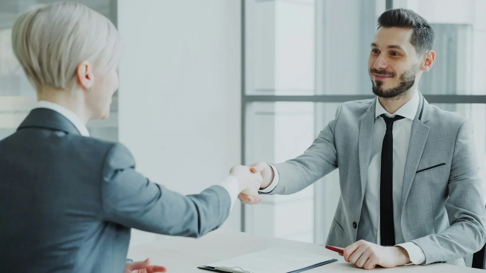 An HR manager shaking hands with a candidate across the table after a job interview