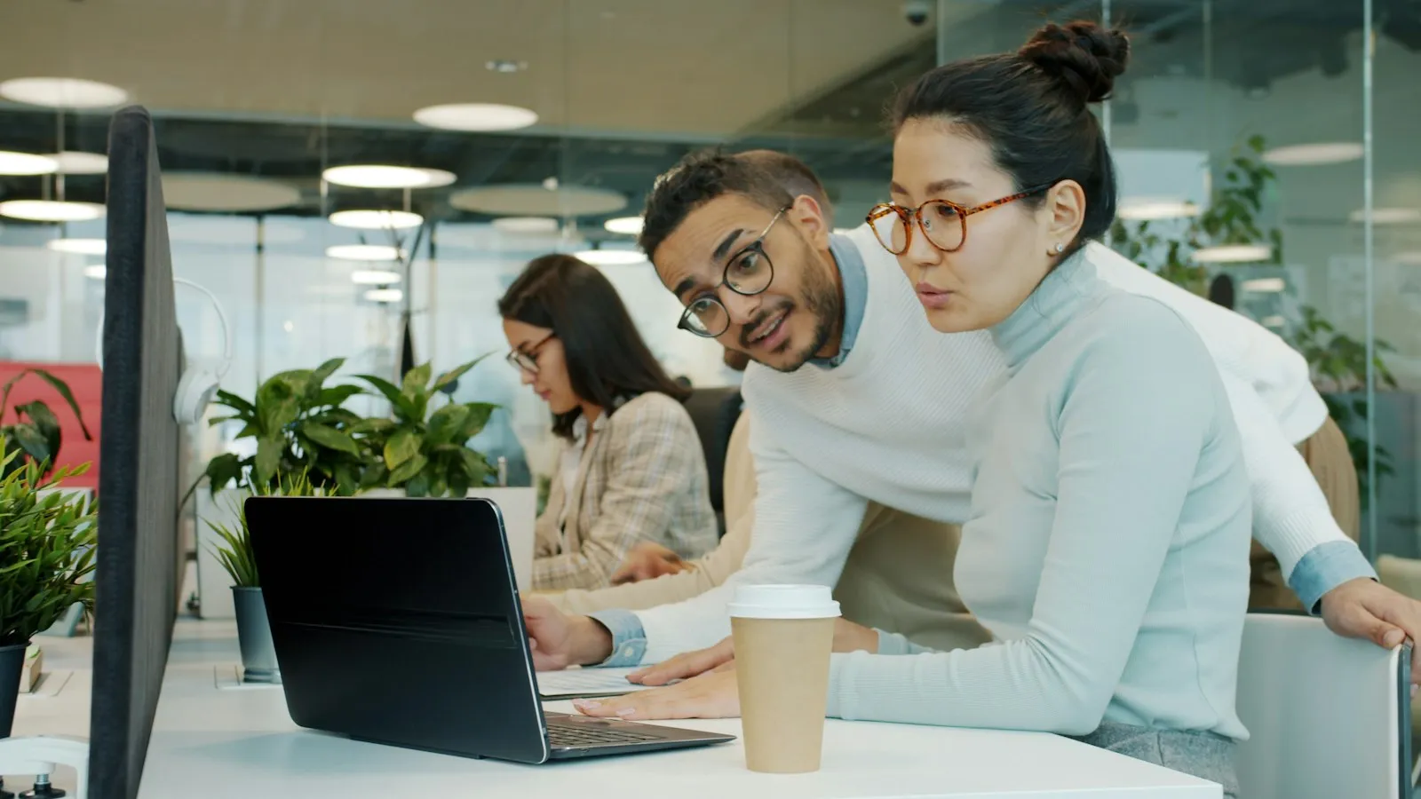 Two colleagues closely reviewing something on a laptop together